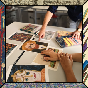 Ausgedruckte Bilder von Paul Goesch liegen auf einem Tisch. 4 Hände von 2 Personen sind zu sehen. Eine Person zeigt auf ein Selbstporträt des Künstler. 