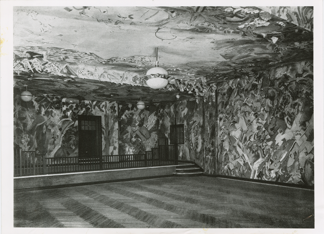 Eine Schwarz-Weiß-Fotografie eines Saals, dessen Wände ornamental, zum Teil auch mit Halbplastiken gestaltet sind. thumbnail