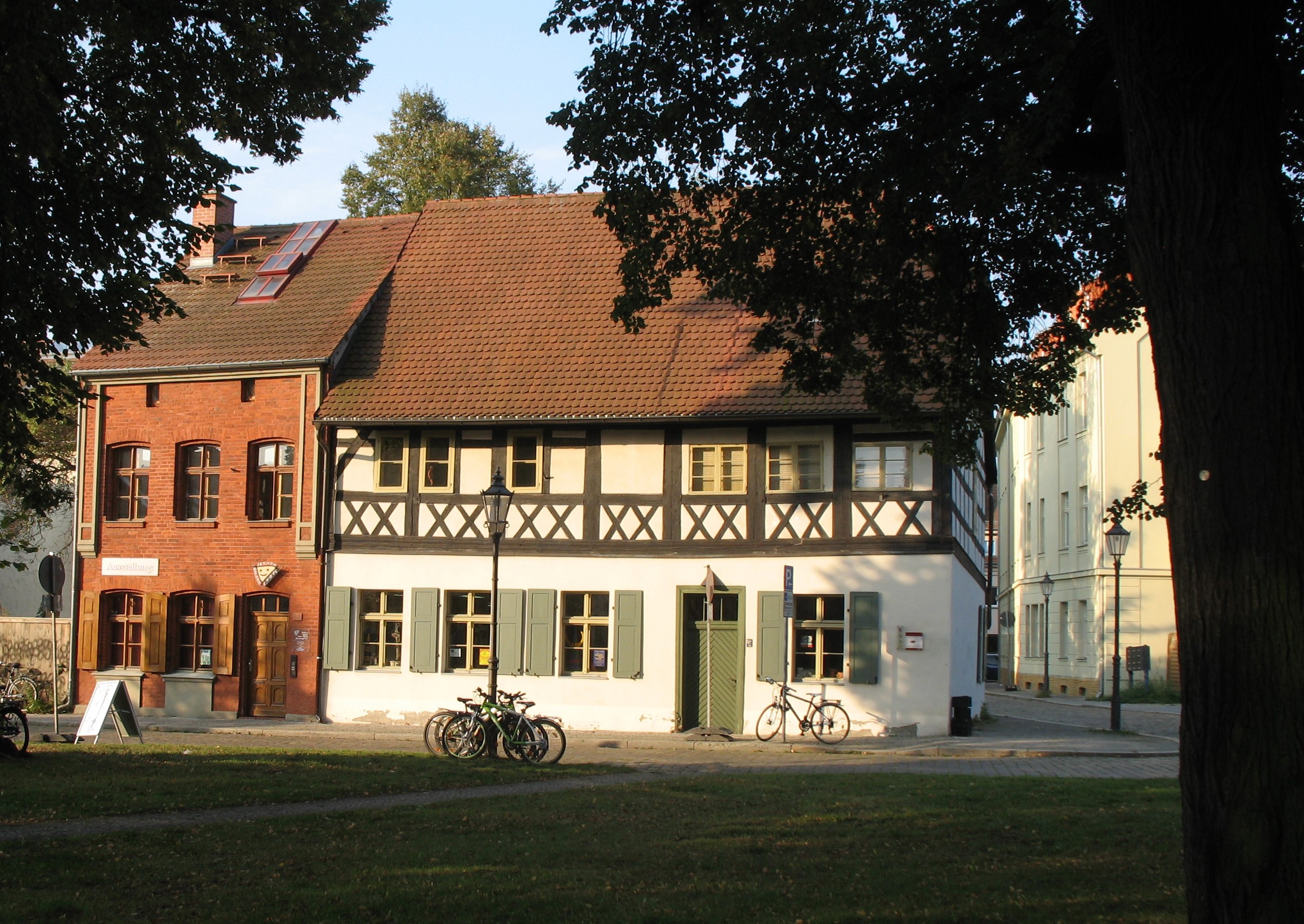 Ein zweigschossiges Fachwerkgebäude neben einem schmalen Haus mit roter Ziegelfassade.