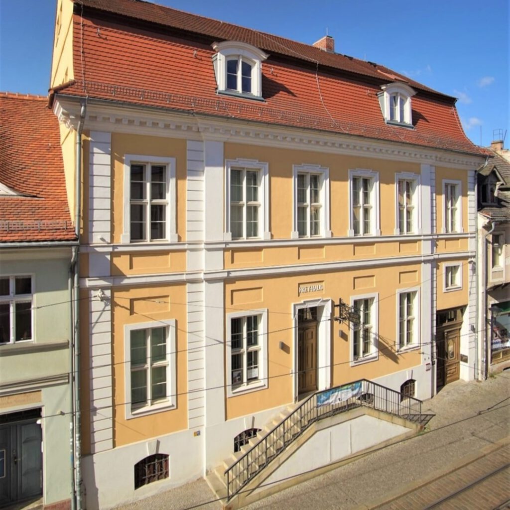 Ein zweigeschossiges Gebäude mit gelber Fassade und einer großen Eingangstreppe.