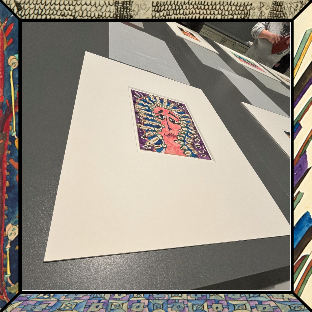 Ein Originalwerk von Paul Goesch liegt auf dem Tisch, auf einem cremefarbenen Passepartout. Es zeigt einen expressionistischen Kof auf blauem Untergrund. Um den Kopf herum ist ein Strahlenkranz, der aus in das Bild gesteckten Streichhölzern besteht thumbnail