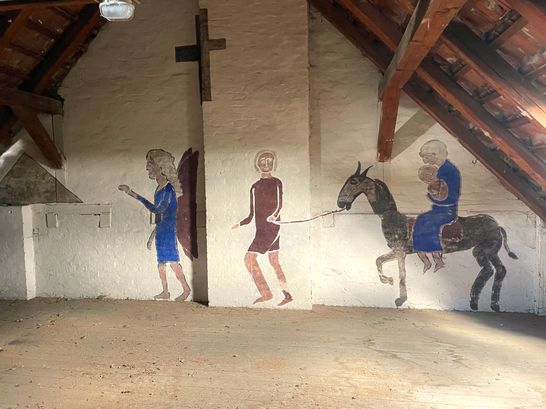 Ein Gemälde von Paul Goesch, das auf einer Wand eines Hauses angebracht ist. Es ist eine Innenwand im Dachgeschoß. Auf dem Wandbild sind ein Engel, eine Person, die einen Esel führt sowie eine Person mit Kind auf dem Arm, die auf dem Esel reitet, zu sehen. thumbnail