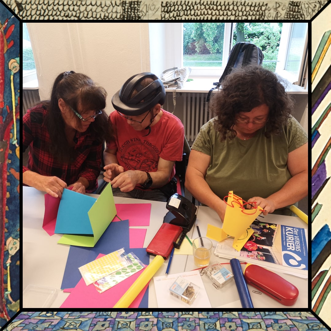 3 Personen sind in einem Workshopraum. Auf dem Tisch vor ihnen liegen bunte Pappbögen. Sie bauen daraus architektonische Entwürfe. thumbnail